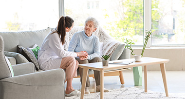 a nurse holding the hand of an elderly lady in a living room sitting on a sofa