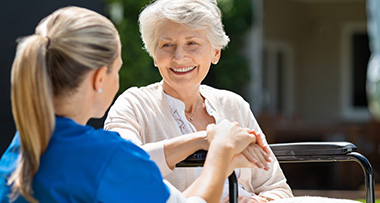 a smiling elderly lady as a nurse holds her hand