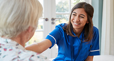 a nurse in blue scrubs with an arm our on an elderly lady's shoulder