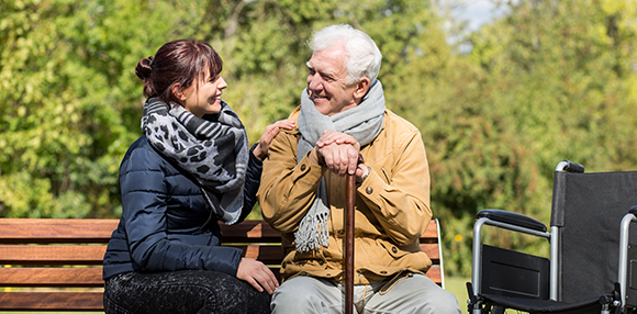an elderly gentleman with a cane sitting on a park bench with a carer smiling