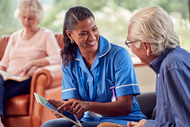 a nurse holding a tablet looking and smiling at an elderly man with glasses