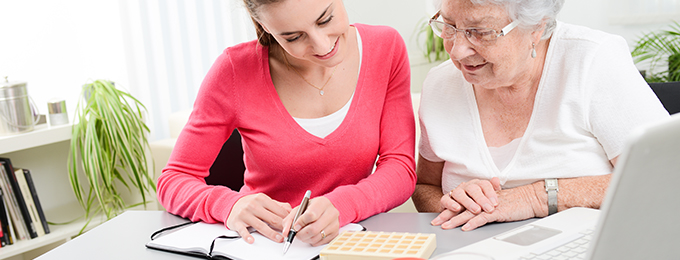 a lady helping an elderly lady organise her medication and writing a plan in a journal 