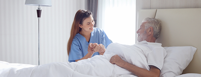 a nurse next to an elderly man in bed holding his hand