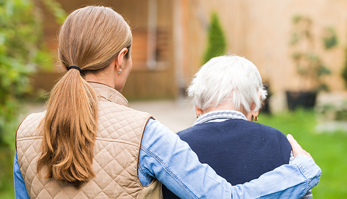 a carer with her arm wrapped over an elderly person walking down a garden]