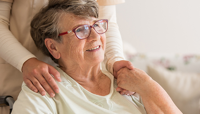 an elderly lady with a carer over standing over her holding each other's hand