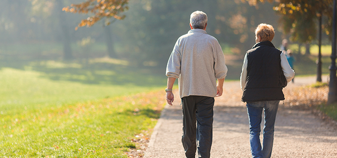 two elderly people walking on a path in a part in autumn