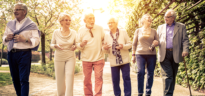 six elderly people walking down a path in a park smiling