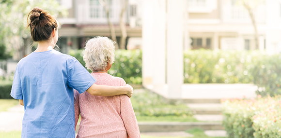 a nurse guiding an elderly lady through a park
